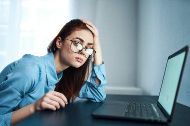 Dizüstü bilgisayarın önündeki mavi gömlekli kadın depresyonda.