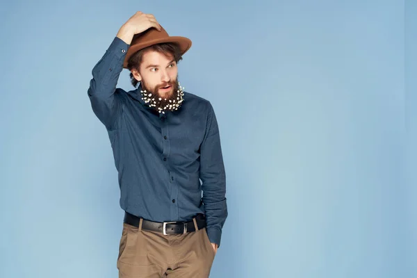 Hombre guapo en sombrero posando flores en barba moda fondo azul —  Fotos de Stock