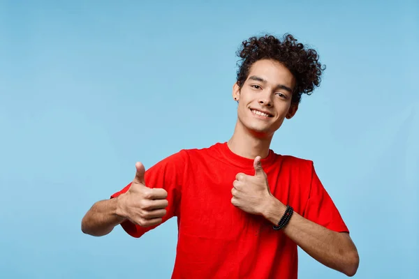 Cheerful guy with curly hair in a red t-shirt gestures with his hands — Stock Photo, Image