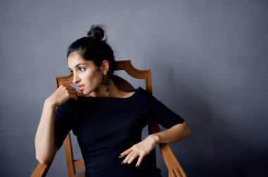 Güzel kadın küpeleri sandalyenin yanında poz veriyor siyah elbise izole edilmiş arka plan.