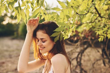 Beyaz elbiseli güzel kadın ağacın yanında poz veriyor.