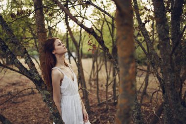 Beyaz elbiseli güzel bir kadın ağaca yaslanıyor. 