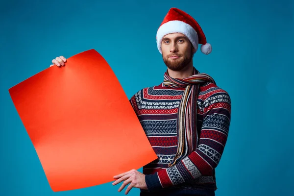 Homme joyeux dans un chapeau de Père Noël tenant une bannière vacances fond bleu — Photo