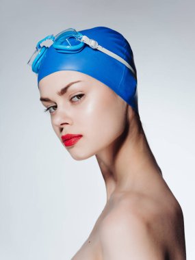 Çıplak omuzlu, yüzme şapkalı, kırmızı dudaklı spor pozu veren bir kadın.