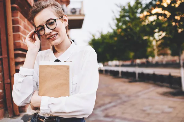 Hezká žena s brýlemi procházky po městě s knihou Životní styl — Stock fotografie