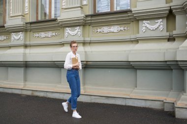 Gözlüklü güzel bir kadın kitap eğitimi alarak şehirde dolaşıyor.