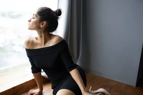 Vacker kvinna i svart klänning nära fönstret poserar elegant stil — Stockfoto