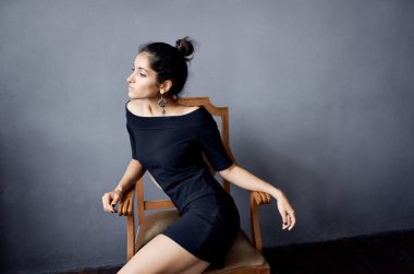 Güzel kadın küpeleri sandalyenin yanında poz veriyor siyah elbise izole edilmiş arka plan.