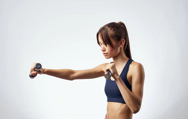 Atletische vrouw fitness oefening halters in de handen van sterke lichte achtergrond — Stockfoto