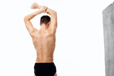 Çıplak vücutlu, şortlu ellerini başının üstünde tutan bir adam. 