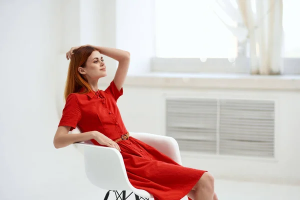 Bela mulher em vestido vermelho sentado em uma cadeira estilo elegante — Fotografia de Stock