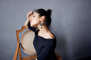 Güzel kadın küpeleri sandalyenin yanında poz veriyor siyah elbise izole edilmiş arka plan.