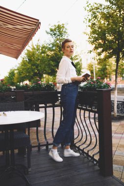 Kısa saçlı kadın yazlık bir kafede dinleniyor.