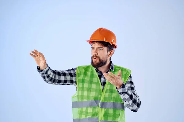 Barbuto uomo verde giubbotto arancione casco flusso di lavoro gesti mano sfondo blu — Foto Stock