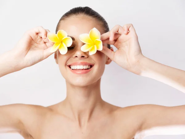 Mujer sosteniendo flores cerca de la cara hombros desnudos fondo claro — Foto de Stock