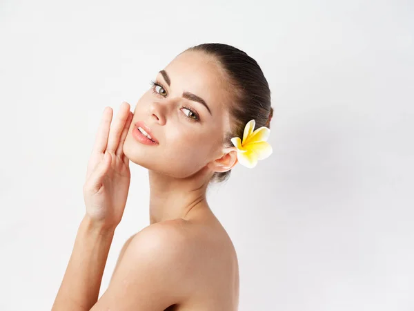 Mujer desnuda hombros cosméticos en flor amarilla en el pelo — Foto de Stock