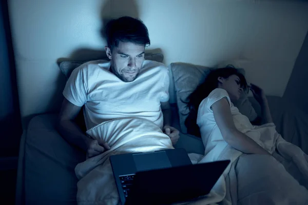 man at night in bed in front of laptop watching movies