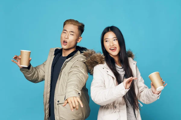 Happy man and woman in warm jackets with a cup of coffee on a blue background — Stock Photo, Image