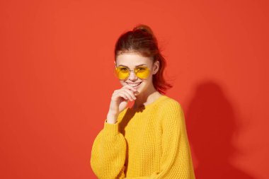 Sarı gözlüklü neşeli kadın başını kırmızı arka planda tutuyor.