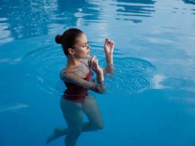 Elleri havada bir kadın havuzda yüzer, dinlenir, tatilde şeffaf su modeli olur.