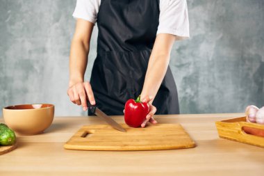 Mutfakta siyah önlüklü bir kadın sebze kesiyor.