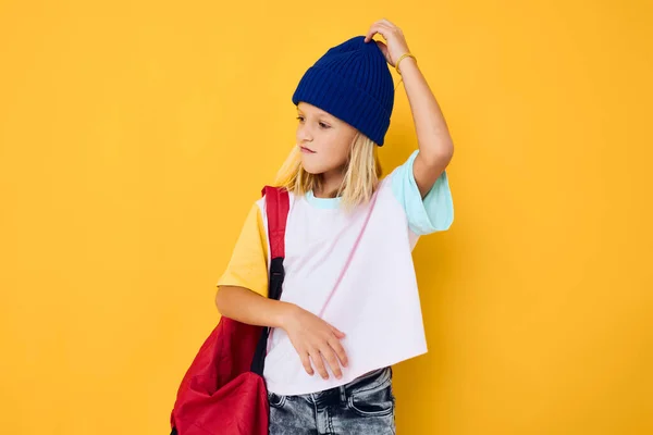 Menina na moda em um chapéu azul mochila vermelha fundo amarelo — Fotografia de Stock