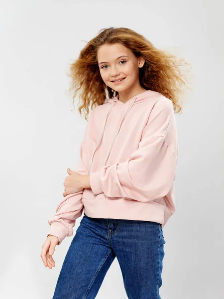 Glückliches Mädchen mit lockigem Haar Rosa Pullover blaue Hose heller Hintergrund — Stockfoto