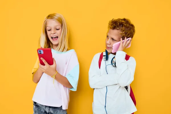 Милые дети со школьными рюкзаками телефон развлечения связи желтый фон — стоковое фото
