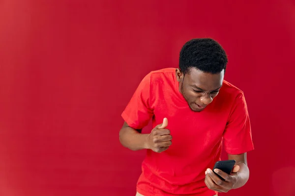 Irritado homem africano olhando para telefone briga estúdio vermelho fundo — Fotografia de Stock