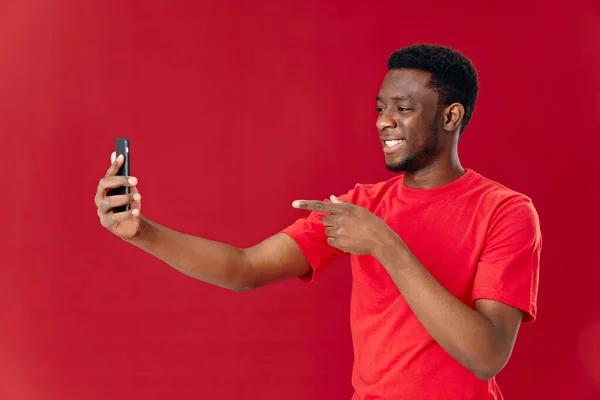 Homem alegre em uma camiseta vermelha com um telefone em suas mãos comunicando emoções — Fotografia de Stock