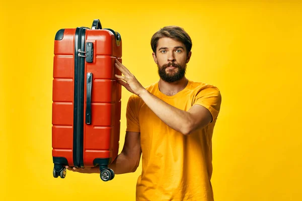 Sarı arka planda kırmızı bavulu ve gür sakallı sevimli bir adam. — Stok fotoğraf