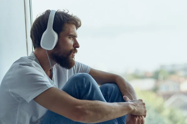 髭を生やした男がヘッドフォンで音楽を聞いて窓の近くに座っていた 高品質の写真 — ストック写真