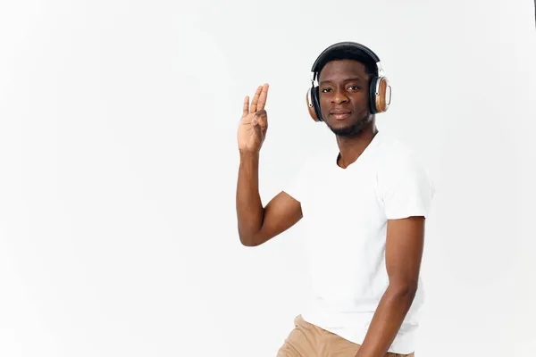 白いTシャツのヘッドフォンでアフリカ系アメリカ人は音楽の手のジェスチャーの光の背景を聞く — ストック写真