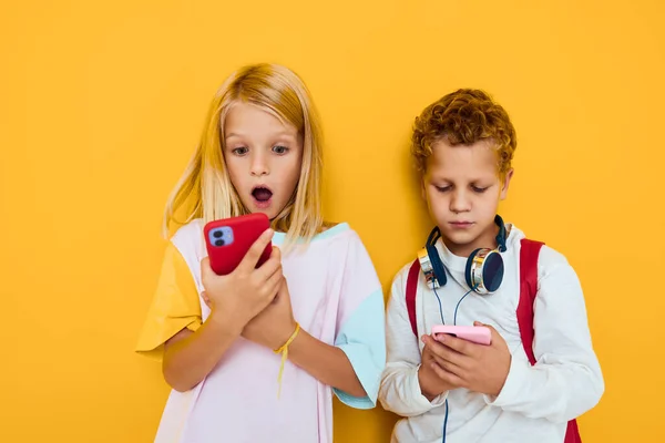Dzieci szkolne używają gadżetów ze słuchawkami żółte tło — Zdjęcie stockowe