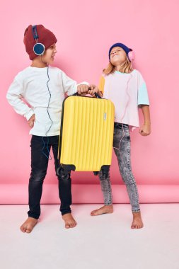 Çocukluk hayat tarzı konsepti kulaklık takan sarı valizli neşeli çocuk ve kız.