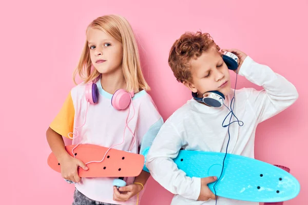 Divertidos niños con auriculares skateboards música moda rosa fondo —  Fotos de Stock