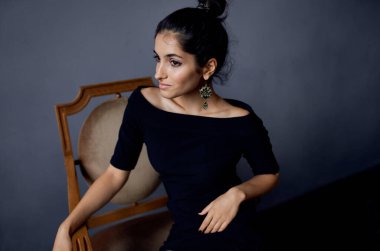 Esmer küpeler, sandalyenin yanında duran mücevherler. Siyah elbise, izole edilmiş arka plan.