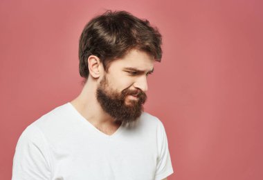 Beyaz tişörtlü sakallı adam hoşnutsuz pembe arka planda kendini ifade ediyor.