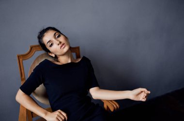 Güzel kadın küpeleri sandalyenin yanında poz veriyor siyah elbise izole edilmiş arka plan.