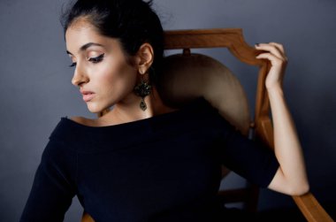 Sandalyenin yanında siyah elbiseli esmer, lüks bir moda stüdyosunun yanında.
