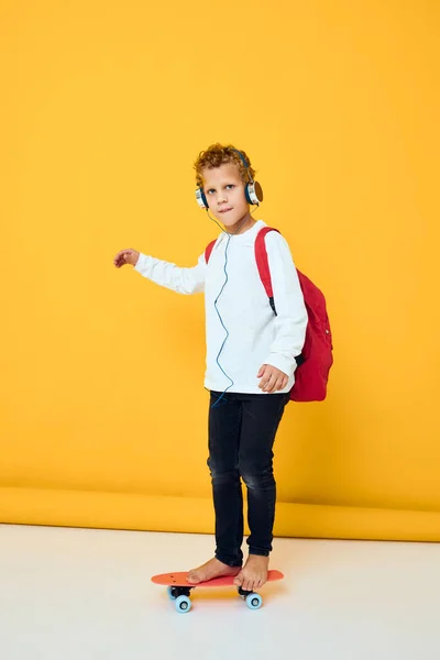 スケートボードのヘッドフォンを身に着けている赤いバックパックを持つスタイリッシュな男の子 — ストック写真