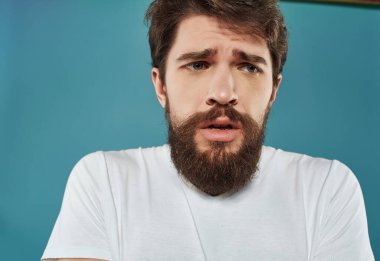 Beyaz tişörtlü sakallı adam öfke stüdyolarını işaret ediyor.