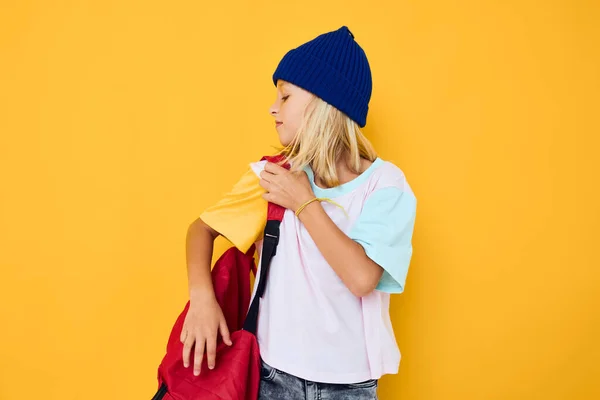 バックパックスクールのある帽子の女の子黄色の背景 — ストック写真