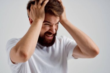 Beyaz tişörtlü, baş ağrısı olan sakallı adam.