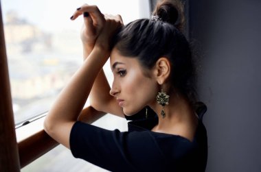 Pencerenin yanında siyah elbiseli güzel bir kadın poz veriyor. 