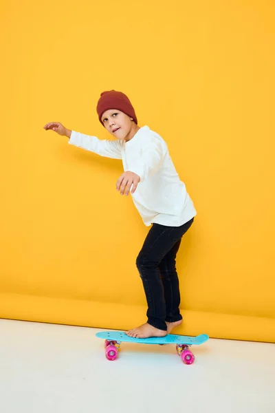 白いセーターの陽気な小さな子供スケートボードエンターテイメント黄色の背景 — ストック写真