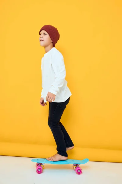 Niño divertido en un monopatín sombrero rojo en sus manos fondo de color amarillo —  Fotos de Stock