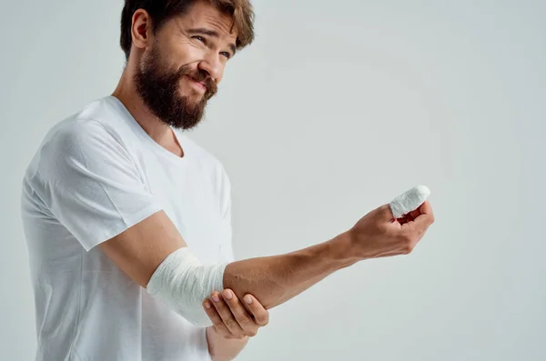 Больной человек в белой футболке с перевязанной рукой, позирующий больничным лекарствам — стоковое фото