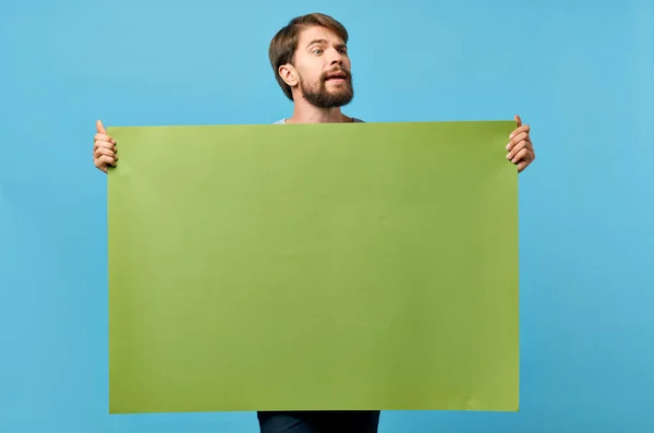 녹색 흉내 내기 포스터를 들고 있는 쾌활 한 남자푸른 배경을 할인하는 모습 — 스톡 사진