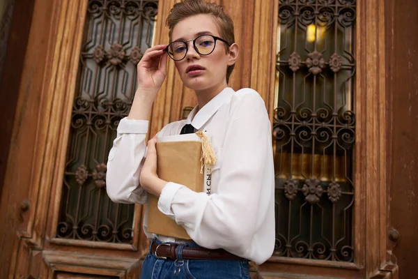 Hübsche Frau mit Brille spaziert mit Buch durch die Stadt — Stockfoto